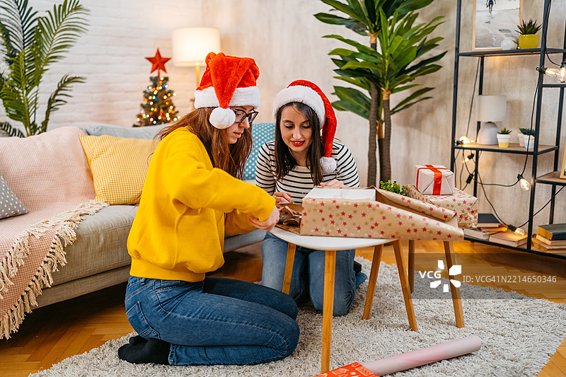 两个年轻女性朋友在客厅里一起包裹圣诞礼物，庆祝圣诞假期。图片素材