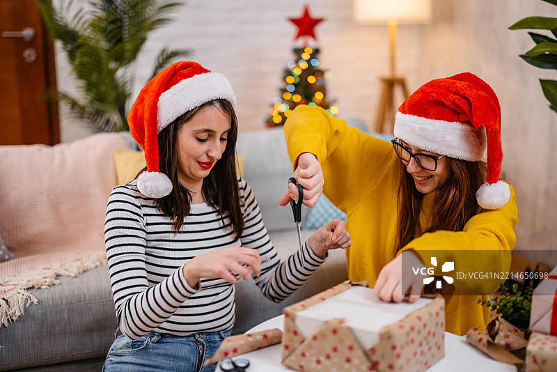 两个年轻女性朋友在客厅一起包裹圣诞礼物，庆祝圣诞假期。图片素材