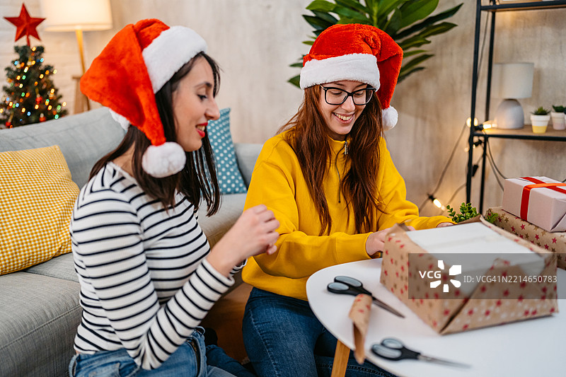 两个年轻女性朋友在客厅一起包裹圣诞礼物，庆祝圣诞假期图片素材
