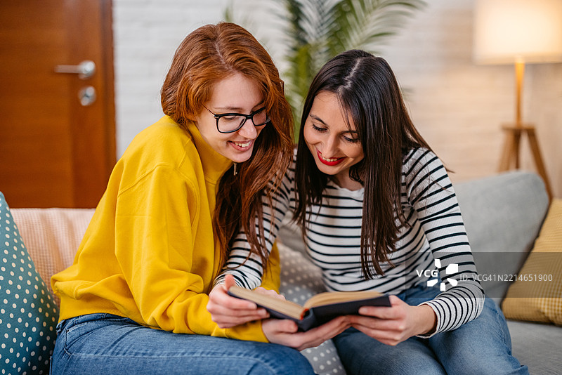 两个女性朋友在家一起阅读一本书图片素材