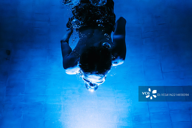 一个男人在傍晚的游泳池中潜水，周围有霓虹灯光。图片素材