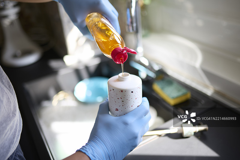 特写镜头：一名男子戴着手套在厨房水槽旁重新填充洗手液分配器图片素材