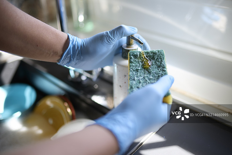 男子在厨房里戴着手套将洗碗液涂抹在海绵上图片素材