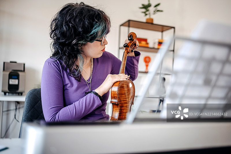 少女在家练习小提琴，停下来调音。图片素材