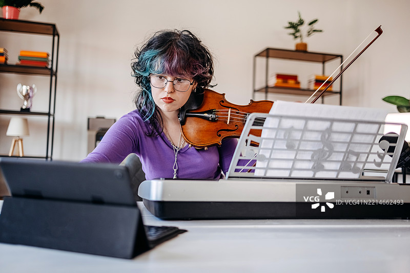 少女在家中坐在笔记本电脑前练习小提琴。图片素材