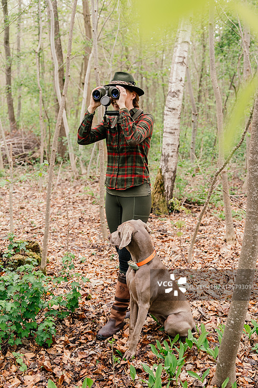 全身照的女性猎人和一只狗在森林中用望远镜观察周围环境图片素材