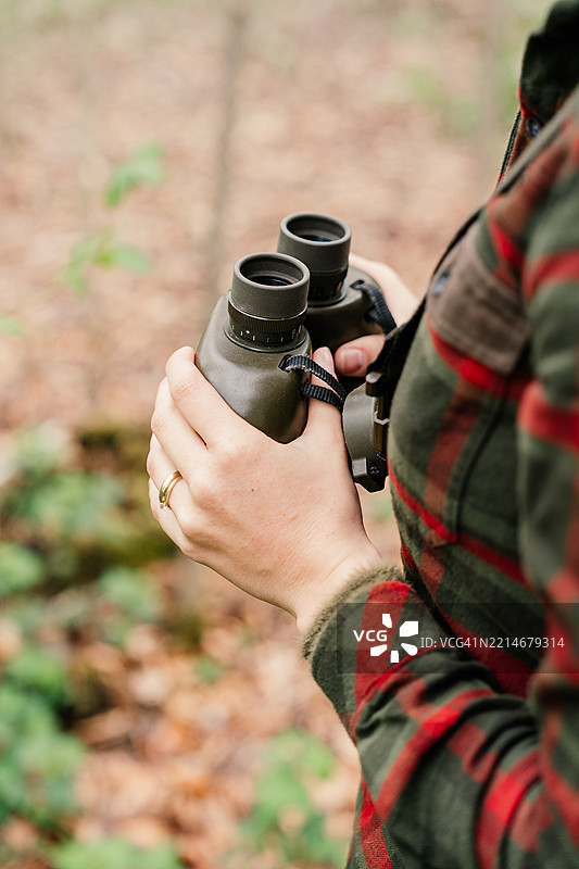 一位女性猎人的手握着望远镜，观察森林中的周围环境。图片素材