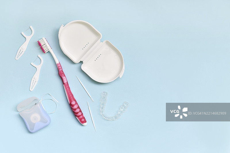 蓝色背景上方视角的牙齿透明矫正器、牙刷、牙签和牙线，留有空白空间。图片素材