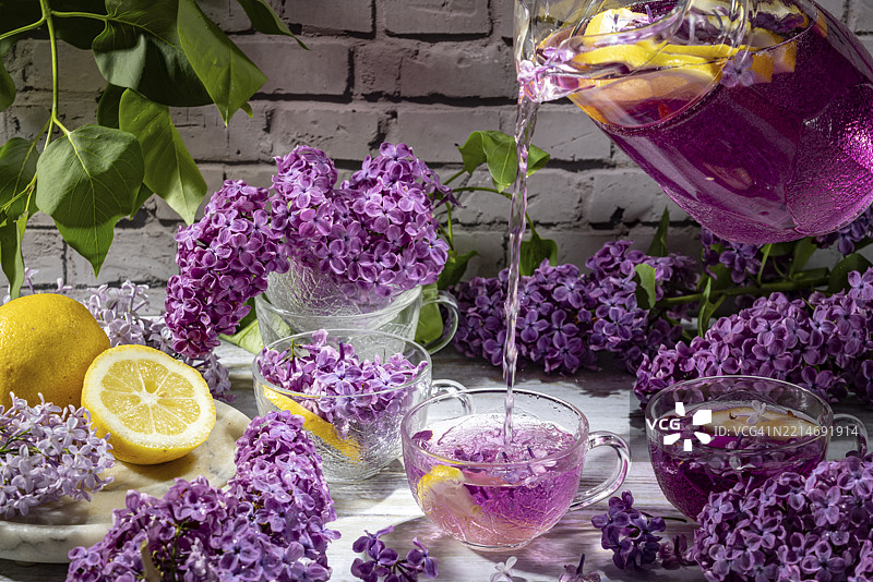 壶正在将紫色饮料倒入杯子，旁边有丁香花和柠檬图片素材