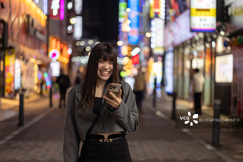 年轻女性下班后在日本居酒屋街游玩，手持智能手机的肖像图片素材