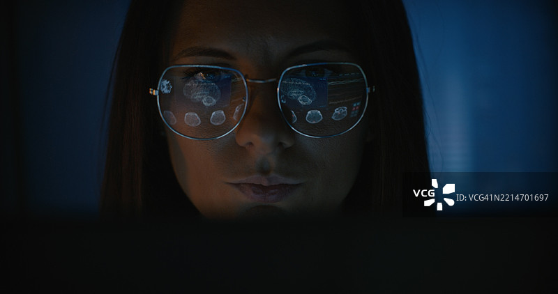 女性科学家在电脑上工作。人类MRI脑扫描的结果显示在电脑屏幕上，反射在眼镜上。医学科学研究。图片素材