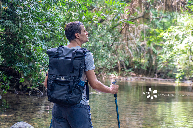 年轻男性徒步旅行者在森林小径上探险，手持登山杖。图片素材
