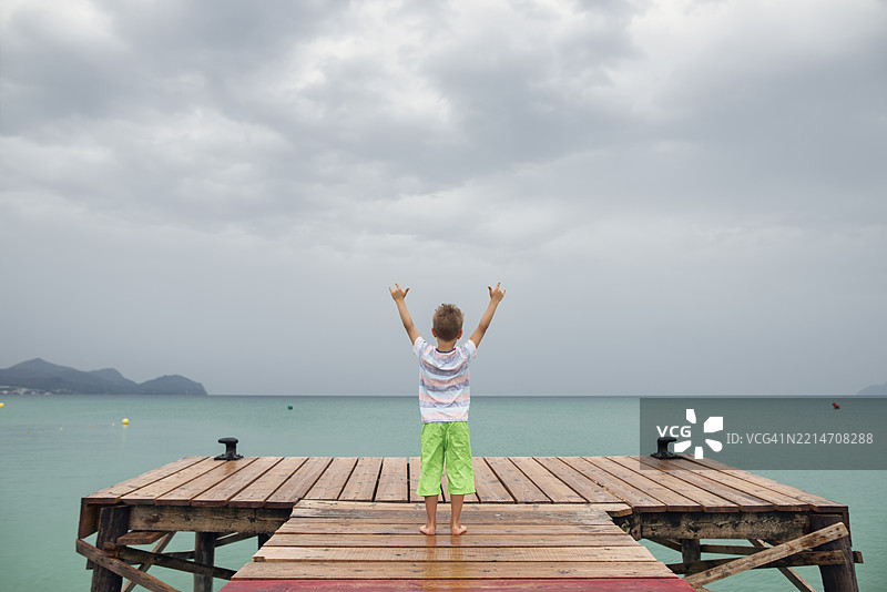 小男孩站在木栈道上，望着阴 cloudy 的海洋。图片素材