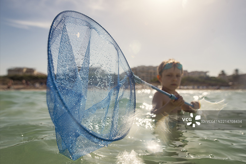小男孩在海中浅水区玩耍，使用渔网捕捉鱼。图片素材
