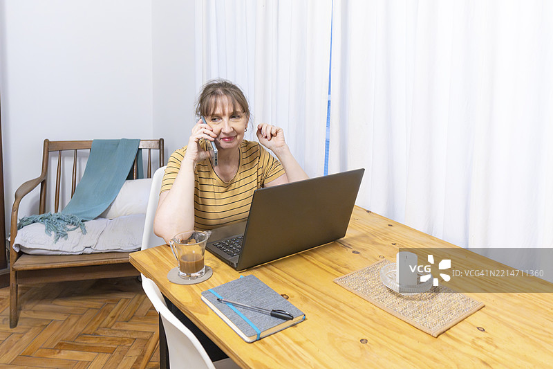成熟的女性在打电话，手边有笔记本电脑和咖啡图片素材
