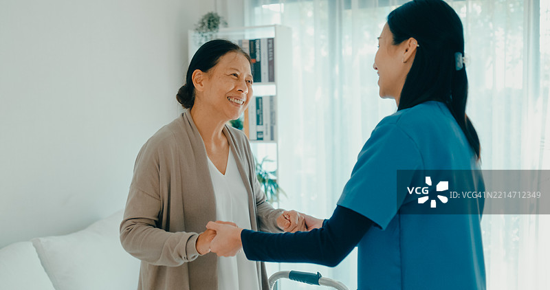 年轻的亚洲护士与一位老年女性在家中的客厅里共享快乐的舞蹈时光，展现了陪伴和积极的生活方式。家庭医疗护理。图片素材