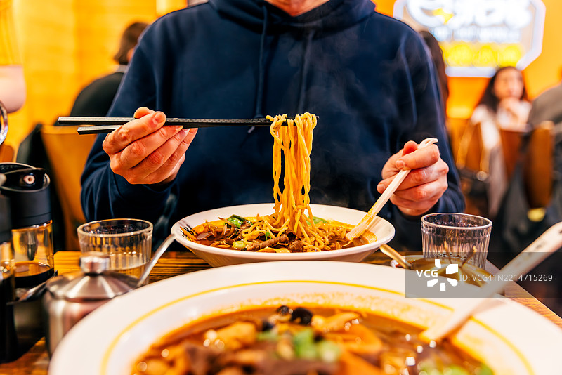餐厅里，一个男人在吃中国面条汤的特写镜头图片素材