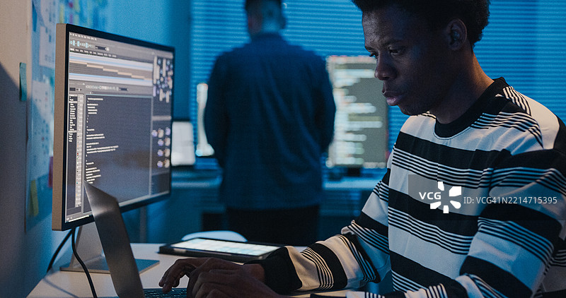 非裔美国男性软件工程师在办公室夜间使用电脑进行程序编码和数据分析。人工智能与编程。图片素材
