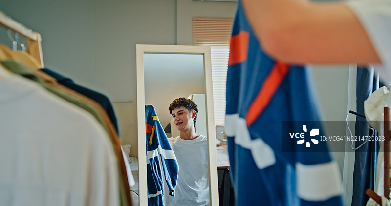 年轻男子自信地选择服装，站在家中卧室的镜子前。健康的早晨生活方式。图片素材