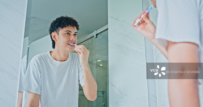 年轻男子在家浴室的镜子前刷牙。健康生活方式的早晨日常概念。图片素材