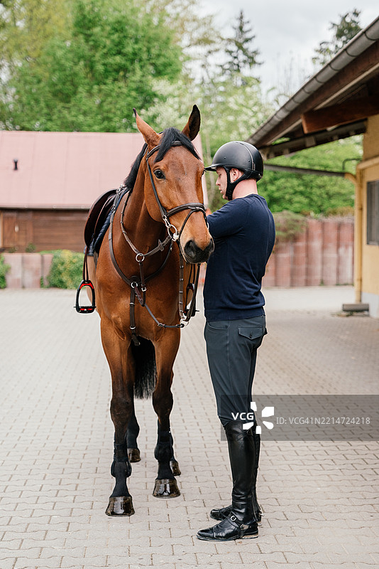 男骑手在马厩前为他的马准备。图片素材