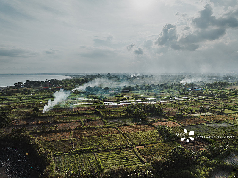 从空中视角拍摄的印尼巴厘岛克隆贡区海岸稻田上升起的烟雾图片素材