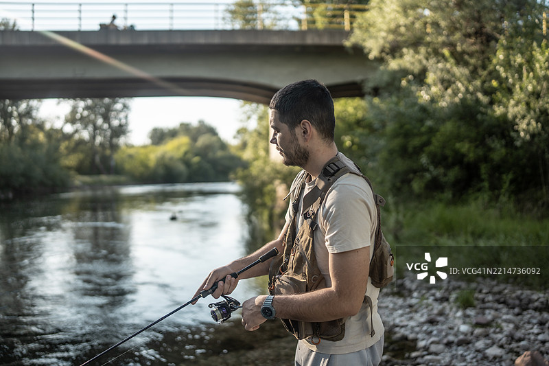 男人在日落时分的桥下宁静河流中钓鱼图片素材