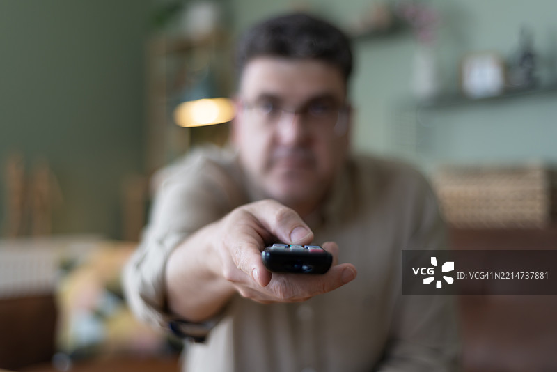 一名男子正在使用遥控器切换智能电视的频道。图片素材