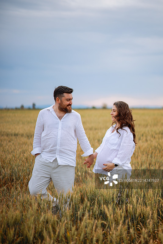 孕妇和她的丈夫手牵手走过草地图片素材