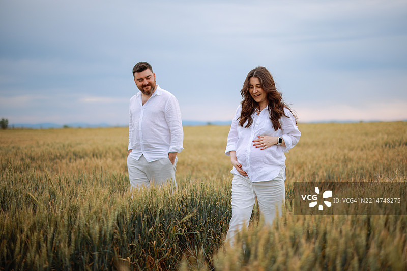 孕妇和她的丈夫手牵手走过草地图片素材