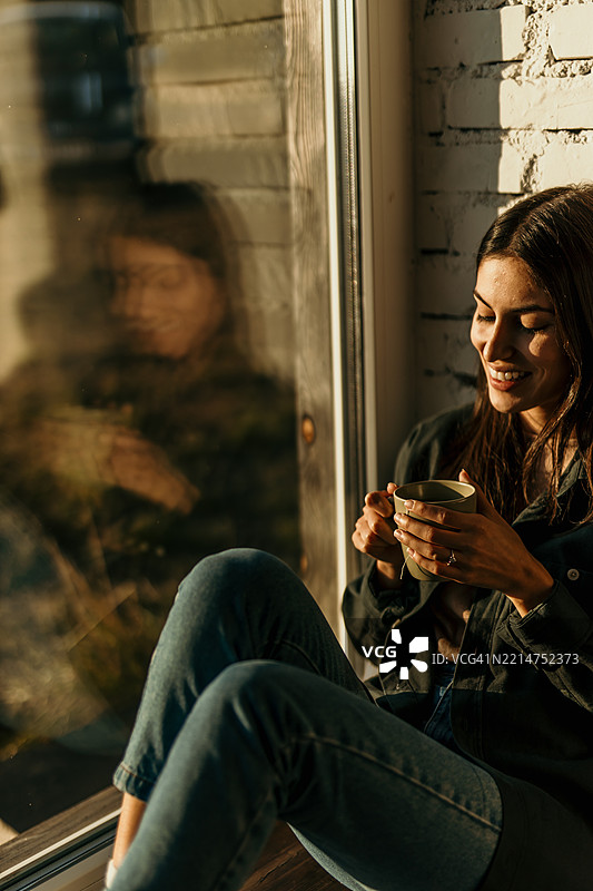 年轻女性在窗边的黄金时刻享受热饮放松身心图片素材