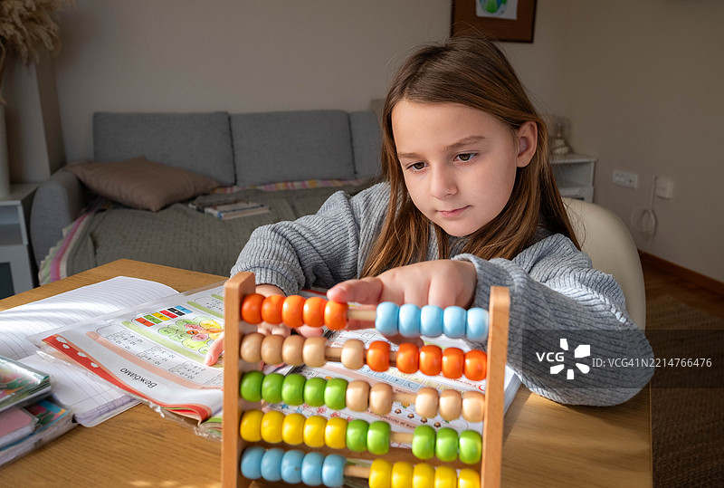 女孩在桌子上学习，使用算盘计算，感到快乐，阅读一本书。图片素材