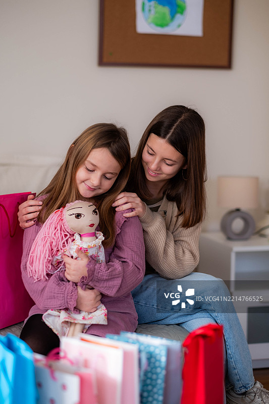 两个快乐的小女孩姐妹坐在沙发上，旁边有购物袋。图片素材