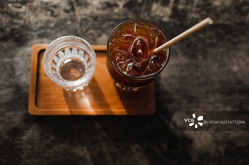 户外咖啡馆木桌上放着一杯清爽的冰咖啡和水，沐浴在日落的光辉中。图片素材