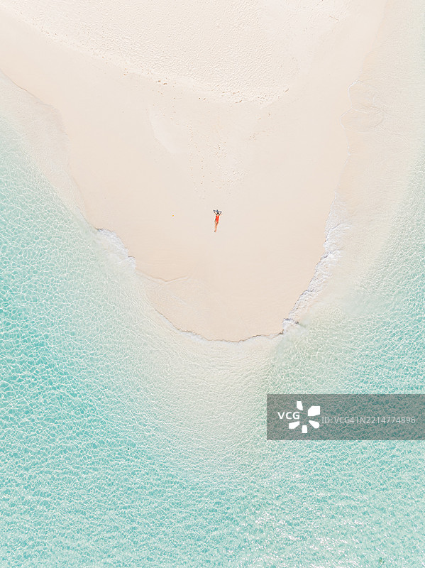 年轻女性躺在热带海滩上的鸟瞰图图片素材