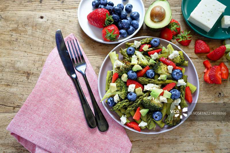 绿色芦笋沙拉配草莓、蓝莓、西兰花和菲达奶酪，摆放在乡村风格的木桌上图片素材