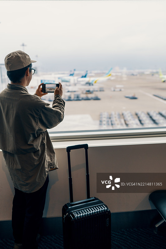 中年男子在机场候机室透过窗户用智能手机拍照图片素材