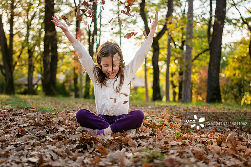 女孩坐在地上玩秋天的落叶图片素材