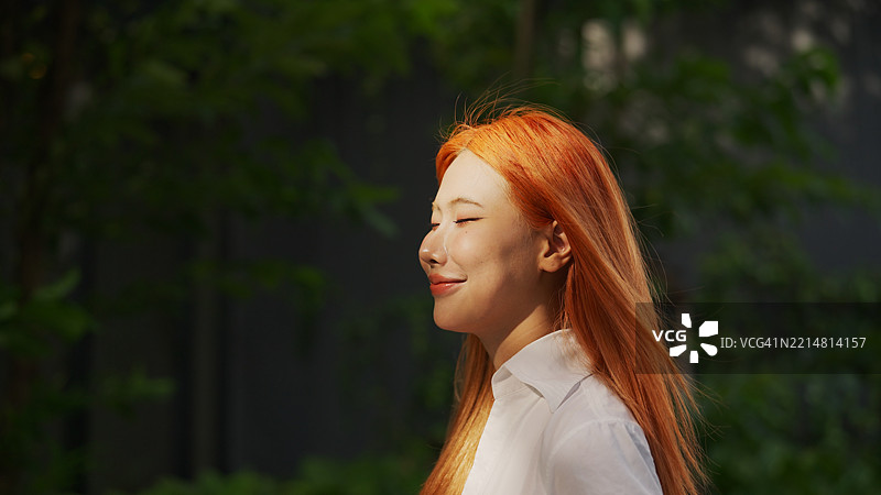 女人宁静的时刻，她的脸上露出微笑，双眼闭合，自然地呼吸着空气。图片素材