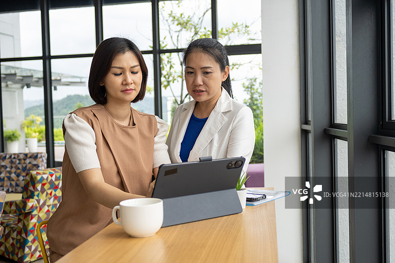 两位亚洲女性正在查看财务交易文件，并用计算器计算开支。图片素材