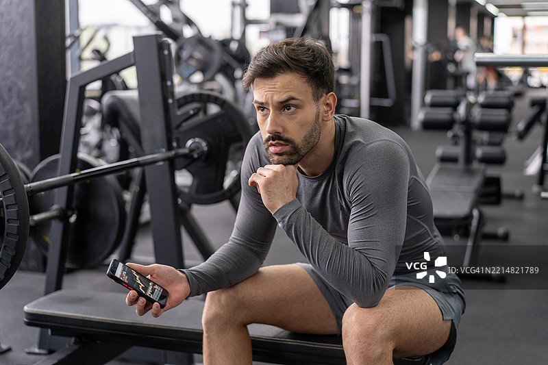 健身后使用智能手机的男子沉思。图片素材