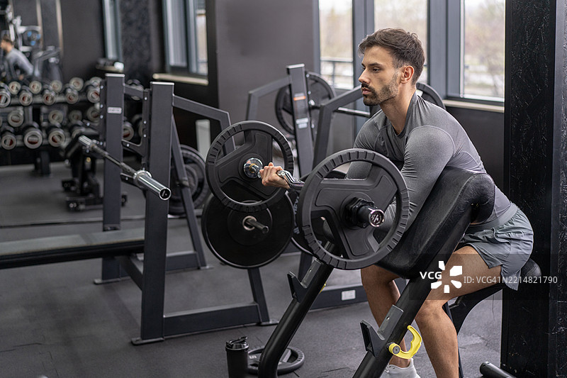 专注的举重运动员正在用杠铃做二头肌弯举图片素材