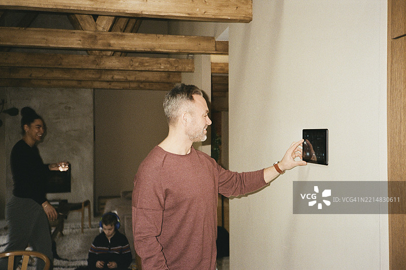 微笑的男子在家中使用挂在墙上的平板电脑图片素材