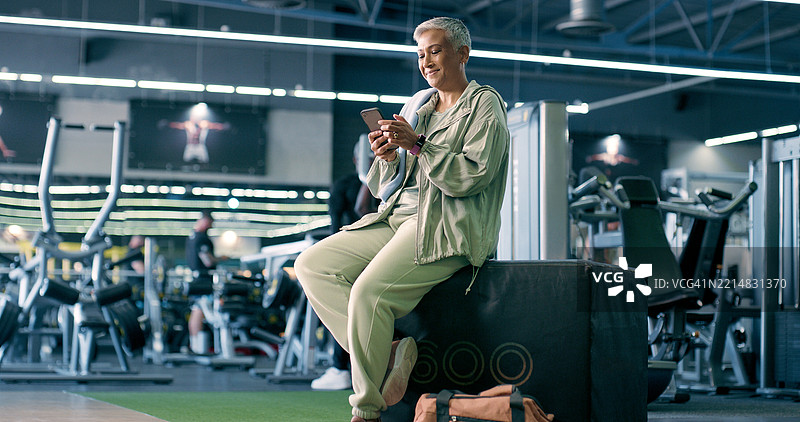 智能手机、健身和健身房中的老年女性，正在休息时使用健康应用程序跟踪健康或心率。移动设备、微笑和运动俱乐部中的人，适用于锻炼计划、训练进度和在线教程。图片素材