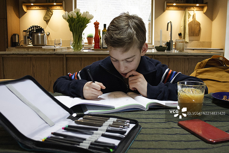 思考的男孩在家里的桌子上摆放着一套彩色铅笔图片素材