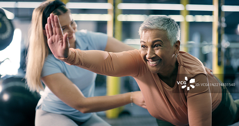 健身房中快乐而成熟的女性私人教练进行锻炼、拉伸以提高灵活性。运动俱乐部，健身教练与个人一起促进健康、活跃和心肺健康的运动。图片素材