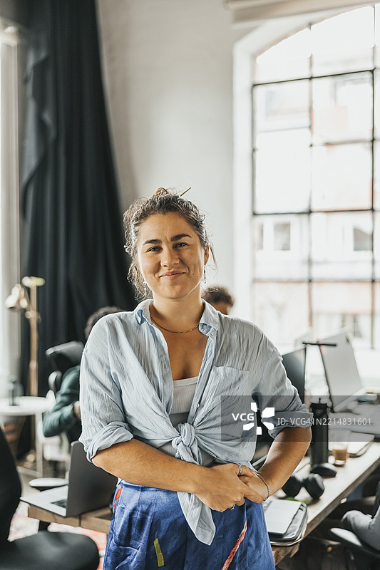 微笑的年轻女性程序员穿着系着衬衫，站在科技初创公司办公室里图片素材