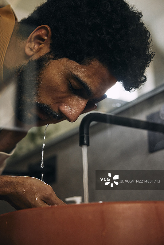 低角度视图的男子在浴室水槽中用水龙头水洗脸图片素材