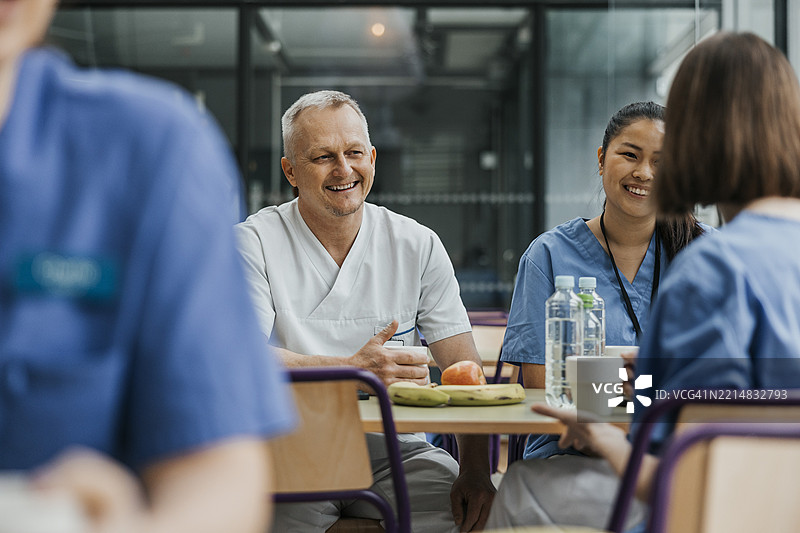 微笑的男性医生在医院自助餐厅与同事们边吃早餐边交谈图片素材
