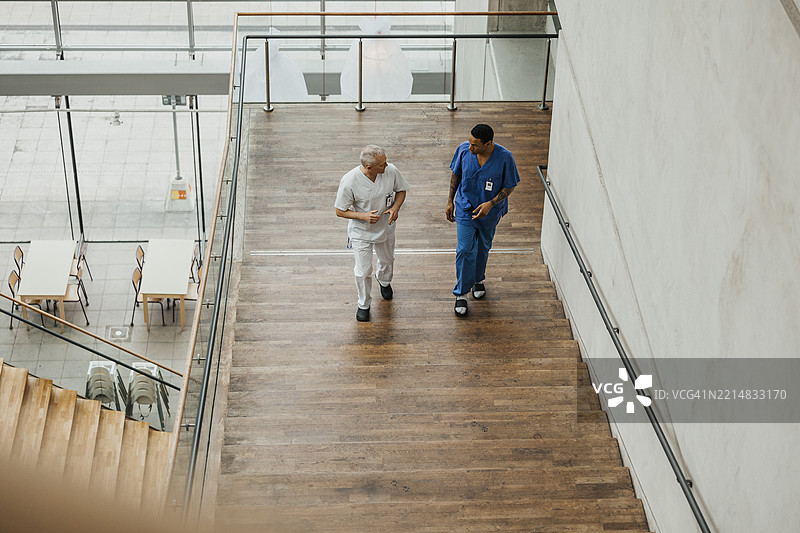 高角度视图的男性医生穿着医用工作服，在医院楼梯上交谈。图片素材